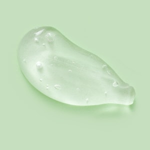 A thick, clear, glossy swatch of transparent shampoo gel with small suspended air bubbles, resting on a solid pale green background.