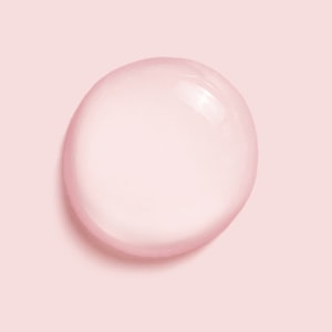 A close-up macro shot of a single, perfectly round drop of clear liquid resting on a solid pastel pink surface.