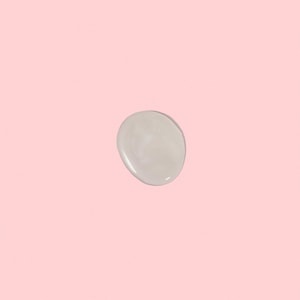 A top-down close-up of a single, thick dollop of pearlescent white shampoo resting gracefully on a solid pastel pink surface.