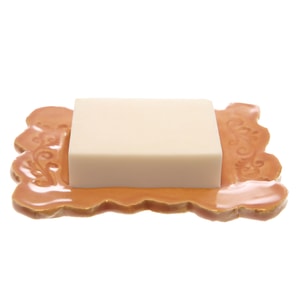 A smooth, rectangular block of opaque white melt and pour soap resting on a decorative, scalloped orange ceramic soap dish against a crisp white background.
