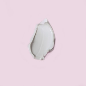 A top-down close-up of a thick, smooth swatch of pale grey mineral face mask resting on a solid pastel pink surface.