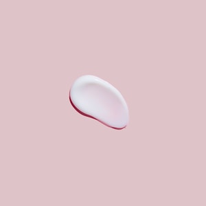 A top-down close-up of a smooth, glossy swatch of white massage lotion resting on a solid soft pink surface.
