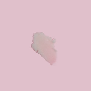 A top-down close-up of a thick, creamy swatch of white granular sugar scrub resting gracefully on a solid pastel pink surface.