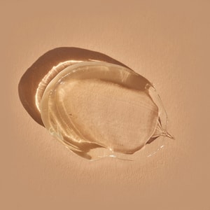 A top-down close-up of a thick, transparent swatch of suspension oil gel casting a distinct shadow on a solid light brown surface.