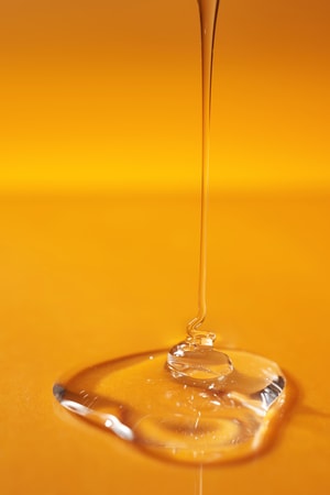 A drop of body gel or shampoo pouring from above on a yellow saturated background.