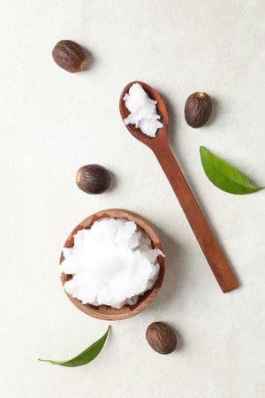 Liquid coconut oil in glass jar, broken coconuts, dark table, se