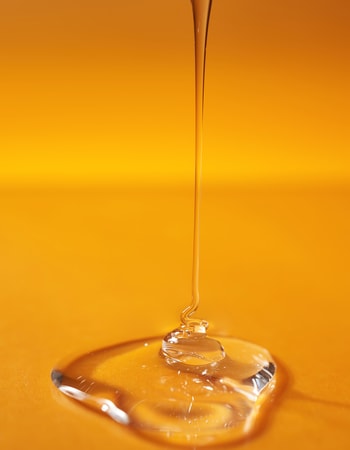 A drop of body gel or shampoo pouring from above on a yellow saturated background.