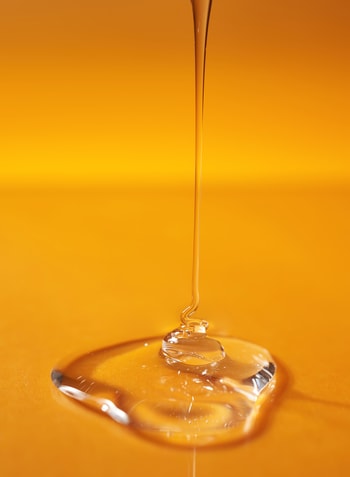 A drop of body gel or shampoo pouring from above on a yellow saturated background.
