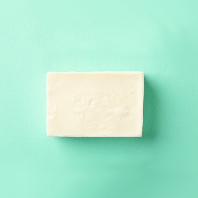 A top-down view of a smooth, rectangular bar of opaque, cream-colored melt and pour soap resting on a bright mint green background.