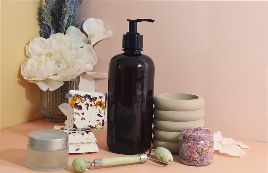 bath and body products on a pink pastel background surrounded by flowers Mother's Day 2025