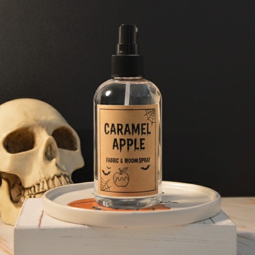 A spray bottle of halloween room spray on a pedistal with a skull behind it.